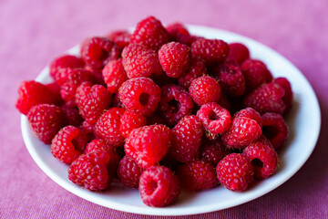 a white plate with raspberries on the table. 