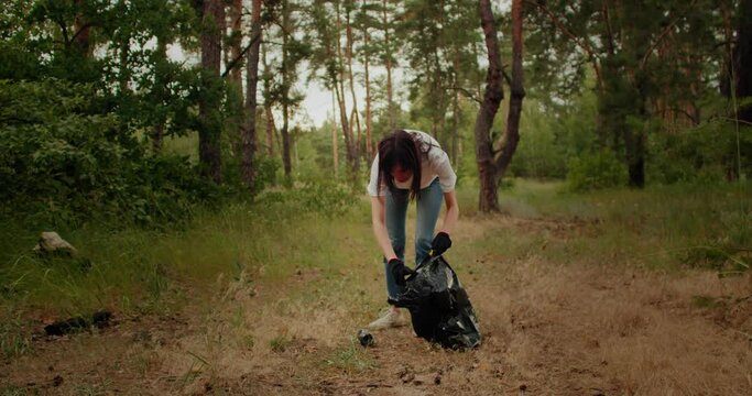 Volunteer woman with garbage bags cleaning forest. Plastic pollution and environmental problem concept.