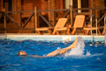 Woman swims in a pool with clear water on the background of a summer sunset on vacation