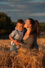 Mom kisses her son on the head in a wheat field at sunset