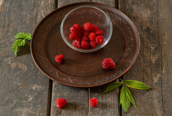 raspberries in a transparent saucer on a ceramic plate on wooden boards. Fruits, food, summer