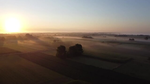 Aerial view of a beautiful misty morning during golden hour above a landscape of farmland and fields with fog