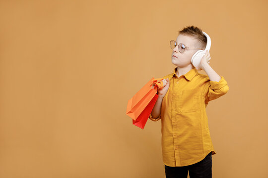 Image of smiling boy holding bags with presents or shoppings on yellow background. child in white headphone. Shopper with many colored paper bags. Holidays sales and discounts. Cyber monday