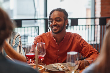 Portrait of young black man talking to friends at table during dinner party in cozy setting