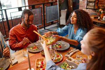High angle portrait of diverse young people enjoying dinner party at table in cozy setting and...