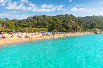 View from a boat of the clear turquoise sea along the Cala Santa Cristina sandy beach on the Costa Brava coast in Lloret de Mar, Spain.