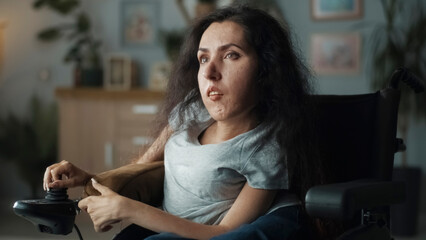Frustrated woman with spinal muscular atrophy sitting in a wheelchair in a dim living room...