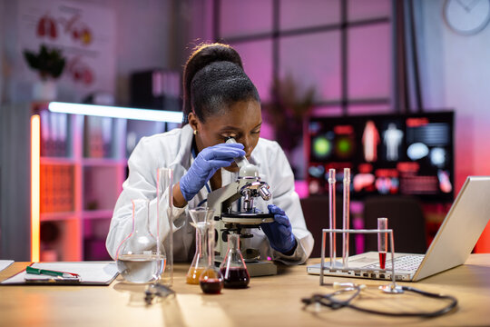 Young african female researcher looking at the microscope observing life science, forensics, microbiology, biochemistry, genetics, oncology, laboratory.