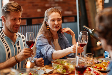 Portrait of young woman enjoying glass of wine while celebrating with friends at dinner party