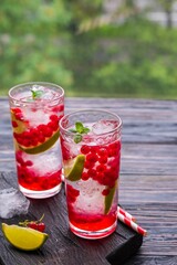 Refreshing drink, lemonade with red currant, lime and ice cubes in glasses on a dark wooden background.