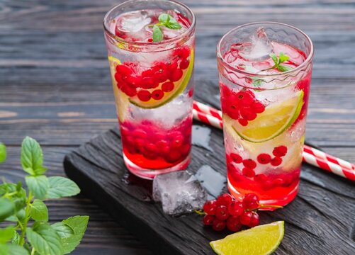 Refreshing drink, lemonade with red currant, lime and ice cubes in glasses on a dark wooden background.