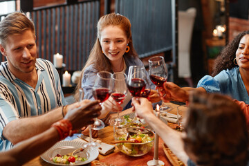 High angle view of young people clinking wine glasses while enjoying dinner party at table in cozy setting