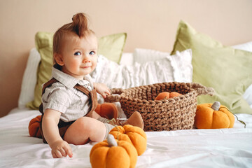 baby with a funny smile is sitting on the bed and playing with stuffed toy pumpkins, Halloween