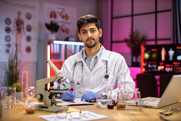 Male scientist working in laboratory. Young indian man researcher supervisor are doing investigations with test tubes while writing research results