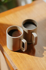 Two coffee cups in warm sunlight on wooden surface