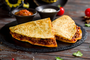 Quesadilla with beef, cheese, bbq sauce and sauces on dark stone plate macro close up