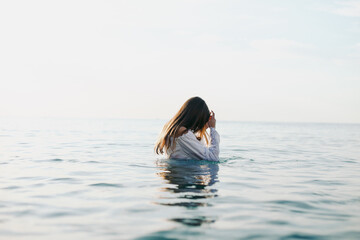 Woman in white dress in water, gentle light, no face