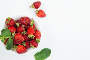 A white plate with strawberries and mint petals stands on the side on a white background close-up, next to it lies mint and several berries with a place for text. High quality photo