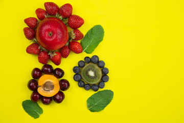 Creative flowers made of fruits and berries decorated with mint leaves on the sides lie on the side on a yellow background with a place for text. High quality photo