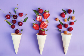 Splash of summer berries from ice cream cones on purple background. Summer time food flat lay