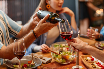 Close up of man pouring wine into glass during dinner party with cozy warm setting