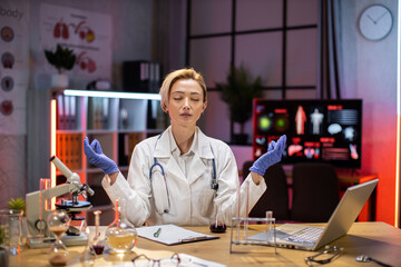 Yong female scientist relaxing practicing yoga wearing lab coat working in laboratory while...