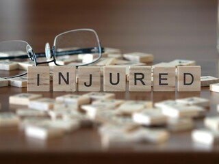 injured word or concept represented by wooden letter tiles on a wooden table with glasses and a book