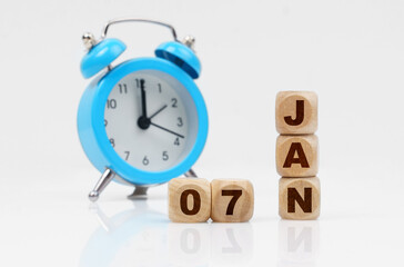 Wooden cube calendar for January 7, next to a blue alarm clock.