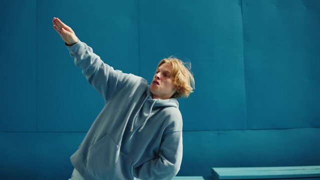 Young man dancing hip hop. Modern dance choreography. Professional breakdancer training on blue background, dancer showing dance movings outdoor. Musical video.