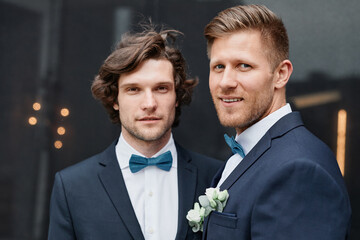 Portrait of two smiling young men wearing suits during wedding ceremony, same sex marriage concept