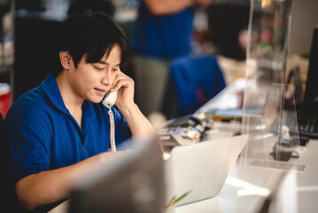 Young male worker focused on working on laptop in a car shop with NFC payment machine on desk to...