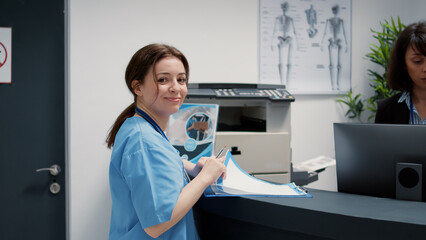 Portrait of medical assistant talking to receptionist at hospital reception counter, having...