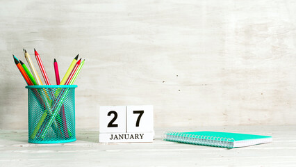 January 27 calendar. The concept of the date of the season. Pencils in a basket against the background of a notebook and the date of the month. Copy space calendar cube.
