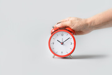 Red alarm clock in female hand on gray background. Close up. Copy space.