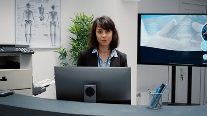 Portrait of receptionist working at hospital reception desk to help people with appointment for...
