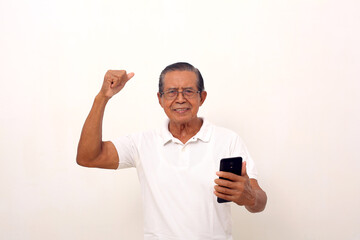 Happy asian old man standing while holding a cell phone and clenching hand. Isolated on white