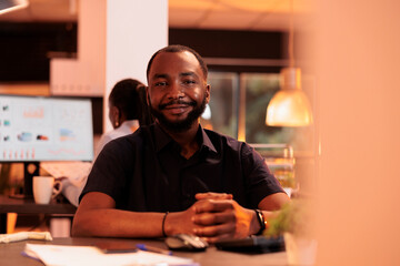 Portrait of young businessman doing paperwork research on computer at office desk, working on web project. Planning report information on pc to create executive presentation online.