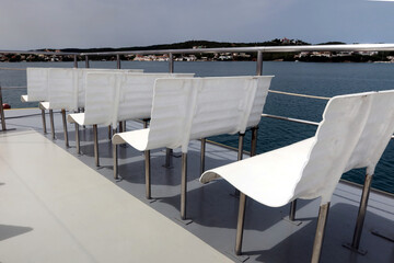 White seats, white chairs on board of a tourist ship; row of white benches on the boat