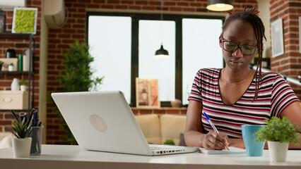 Business student taking notes at online webinar class on laptop, doing remote work and distant...