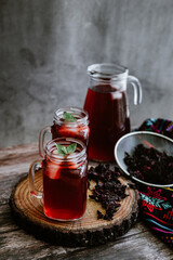 Agua de Jamaica or roselle mocktail drink, summer beverage in mexico with ice and dry hibiscus petals on table background	
