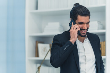 Hispanic smiling businessman in white shirt and blazer making a call on smartphone working at home. Indoor shot. High quality photo