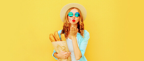 Portrait of young woman blowing her lips sending air kiss holding grocery shopping paper bag with...