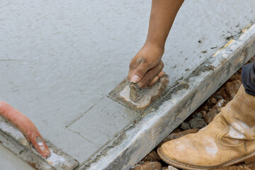 This construction worker is holding a steel trowel and smoothing out the plastering of new sidewalk...