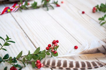 Obraz na płótnie Canvas Branches of lingonberries and feathers on a white wooden background