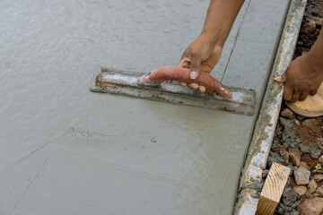 A construction worker is working on a new sidewalk that has just been poured on wet concrete while holding steel trowel