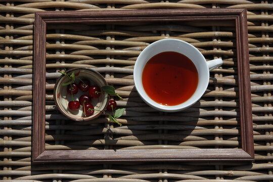 A tableau in a wooden frame with a white tea cup and cherry berries standing on the surface with a woven pattern in the street design of the restaurant.The concept of ecological healthy nutrition