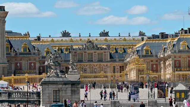 Stunning footage of the facade of the palace of Versailles: the golden details capture the attention of the observer with their beauty. Swarming with people coming and going to visit. Sunny day