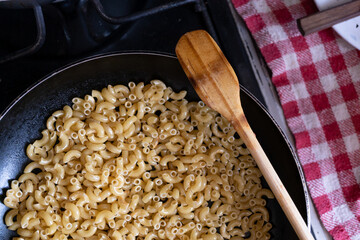 friendo pasta de coditos en sartén de teflón con palita de madera