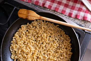 friendo pasta de coditos en sartén de teflón con palita de madera