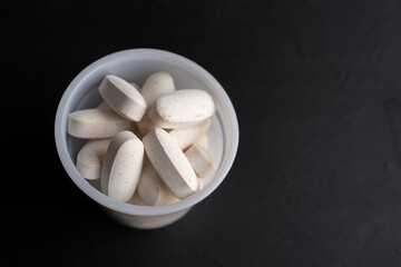 bote de plástico lleno de comprimidos o pastillas de calcio y colágeno hidrolizado sobre fondo negro 